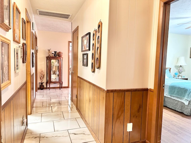 corridor featuring light wood-type flooring, wooden walls, and a textured ceiling