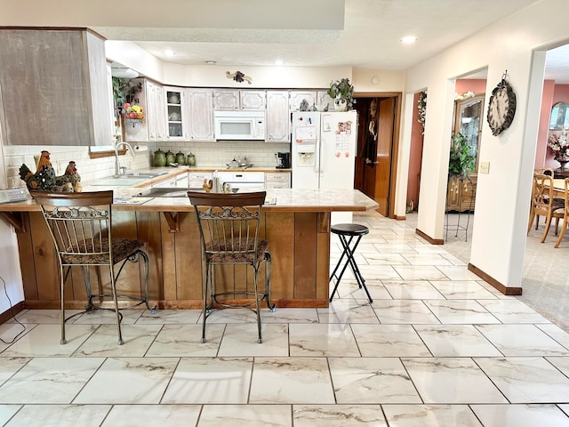 kitchen featuring white cabinetry, sink, kitchen peninsula, a kitchen breakfast bar, and white appliances