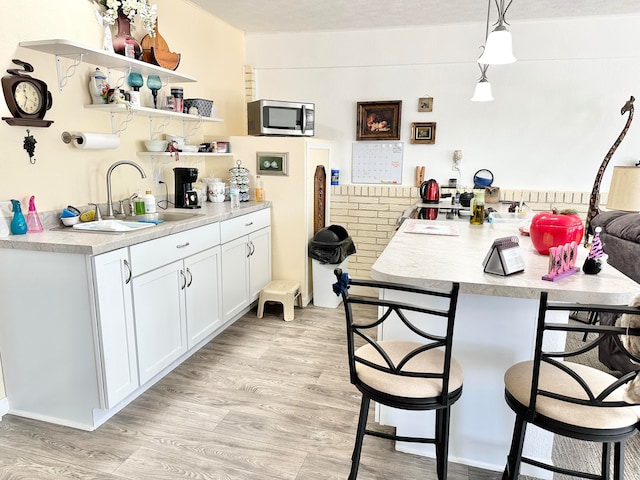 kitchen featuring white cabinetry, pendant lighting, sink, a breakfast bar area, and light hardwood / wood-style flooring