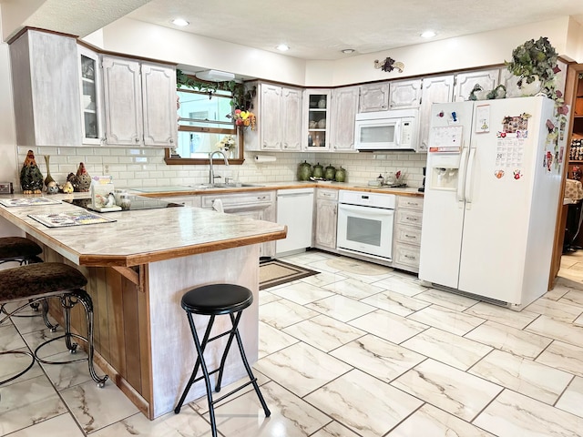 kitchen featuring kitchen peninsula, a breakfast bar area, tasteful backsplash, sink, and white appliances