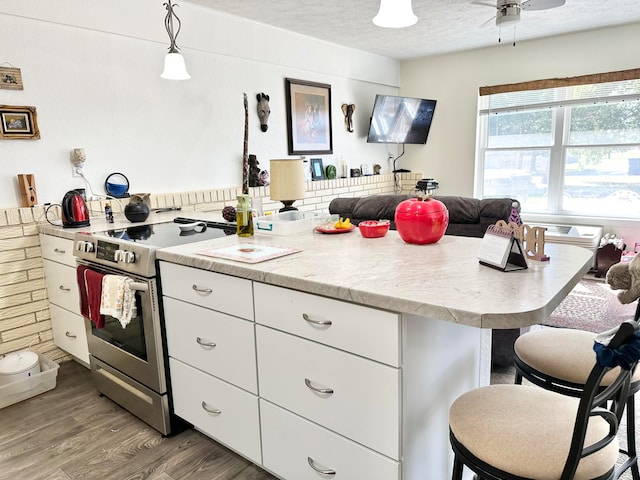 kitchen with hanging light fixtures, white cabinetry, and stainless steel electric range oven