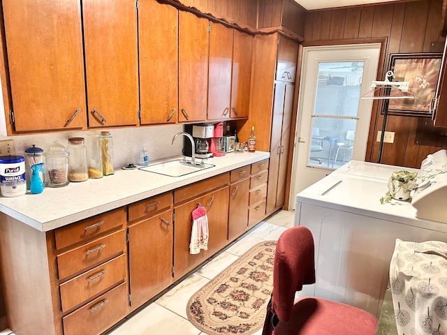 kitchen with light tile patterned floors, wood walls, sink, and washing machine and clothes dryer