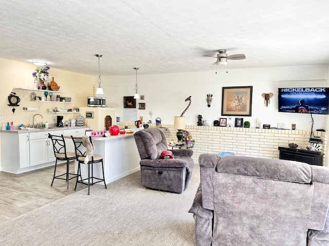 living room with ceiling fan, a textured ceiling, sink, and light wood-type flooring