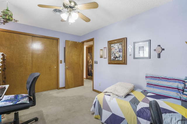 bedroom featuring a textured ceiling, ceiling fan, a closet, and light colored carpet