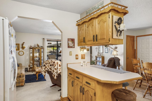 kitchen featuring a textured ceiling, kitchen peninsula, white fridge, and light colored carpet