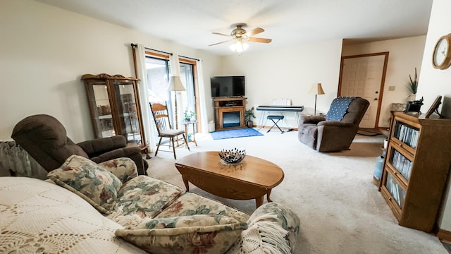 living room with a glass covered fireplace, a ceiling fan, and carpet flooring