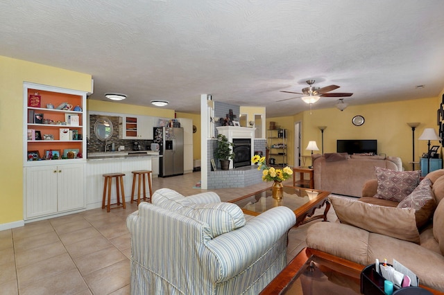 tiled living room featuring a fireplace, a textured ceiling, and ceiling fan