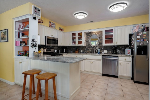 kitchen with tasteful backsplash, white cabinets, kitchen peninsula, appliances with stainless steel finishes, and a kitchen breakfast bar