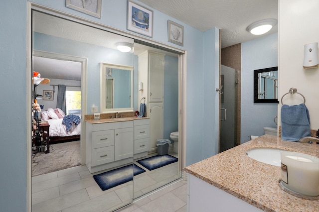 bathroom featuring tile patterned flooring, a shower with shower door, vanity, and toilet