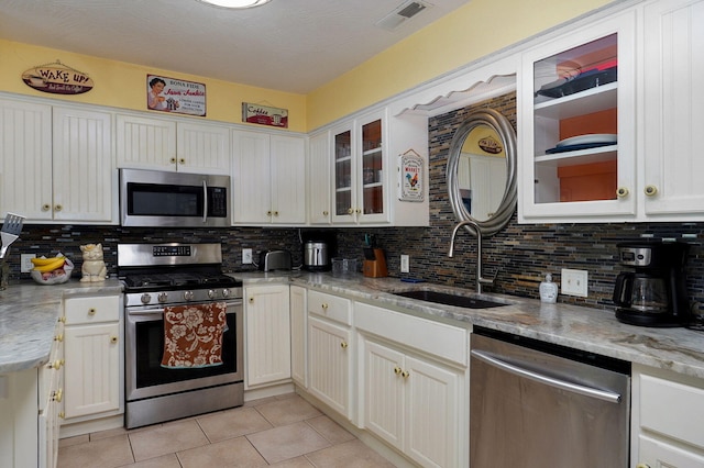 kitchen featuring sink, backsplash, white cabinetry, appliances with stainless steel finishes, and light stone countertops