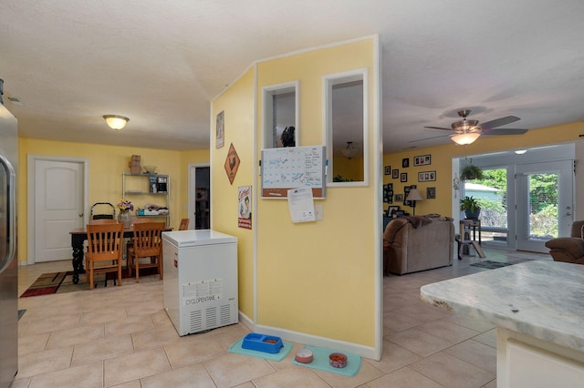 interior space with ceiling fan, refrigerator, light tile patterned floors, and a textured ceiling