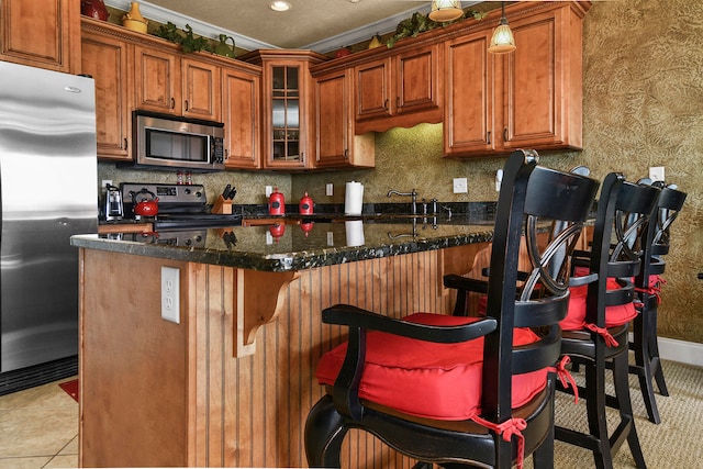 kitchen with pendant lighting, light tile patterned floors, appliances with stainless steel finishes, a breakfast bar, and dark stone countertops