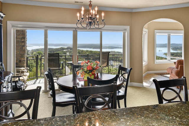 dining space featuring a notable chandelier, carpet, ornamental molding, and a water view