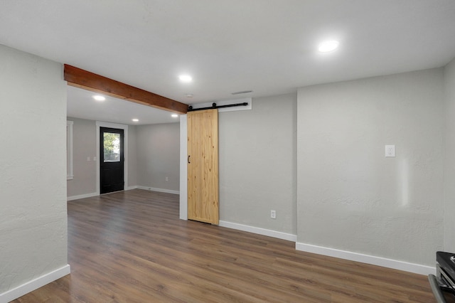 empty room featuring a barn door, beam ceiling, and dark hardwood / wood-style flooring