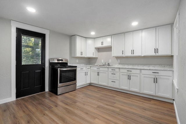 kitchen with light stone countertops, sink, white cabinetry, light hardwood / wood-style flooring, and electric range