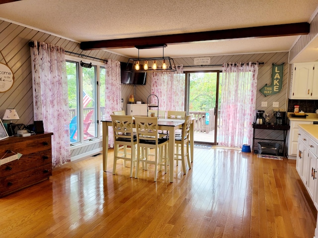 dining space featuring wood walls, beamed ceiling, and a wealth of natural light