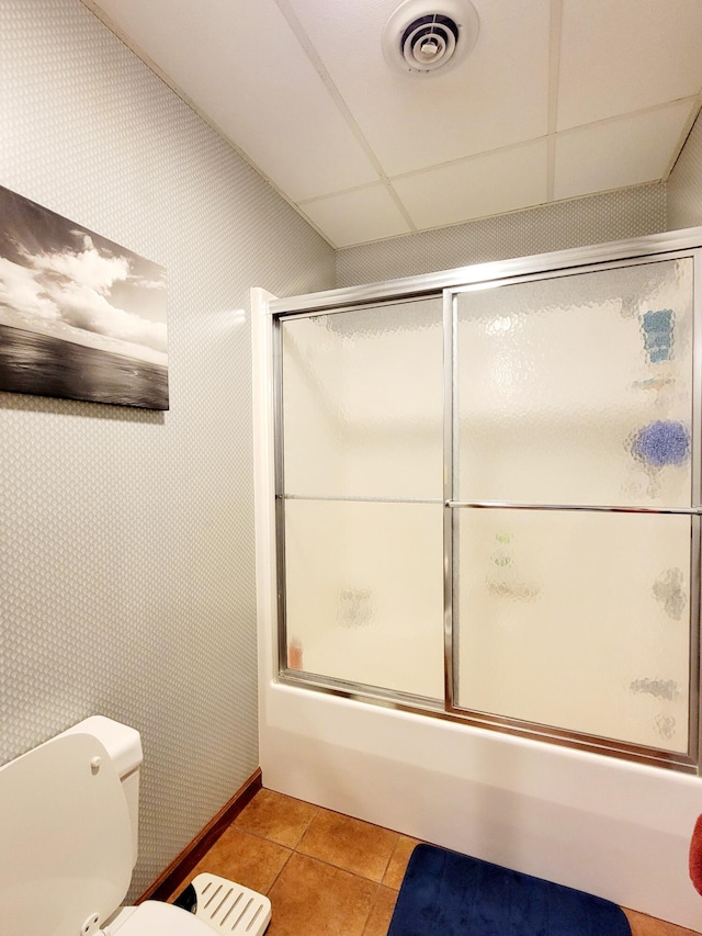 bathroom with tile patterned floors, a drop ceiling, bath / shower combo with glass door, and toilet