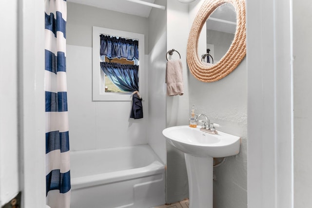 bathroom featuring a textured wall, a sink, and shower / bath combination with curtain