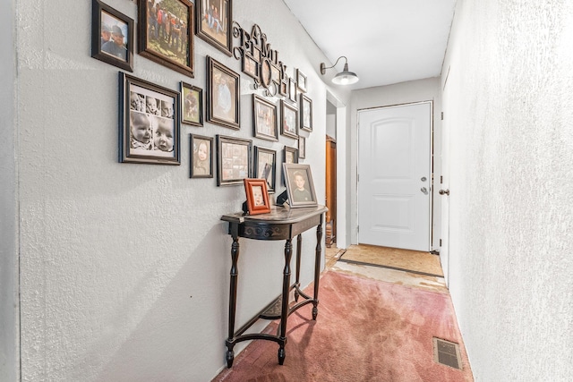 doorway featuring a textured wall, visible vents, and carpet