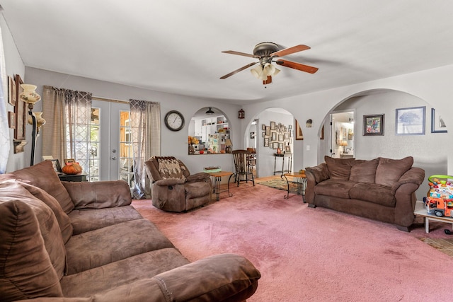 living area with ceiling fan, arched walkways, french doors, and carpet