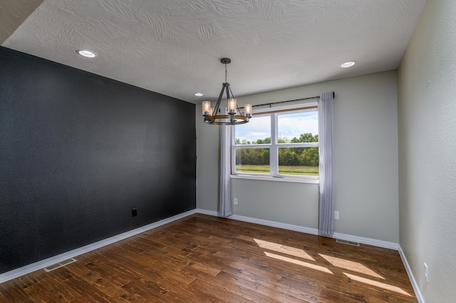 unfurnished room featuring a notable chandelier, dark hardwood / wood-style floors, and a textured ceiling