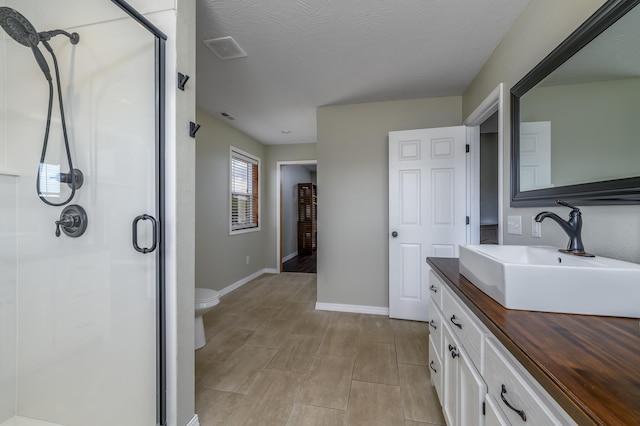 bathroom featuring vanity, a shower with shower door, toilet, and a textured ceiling