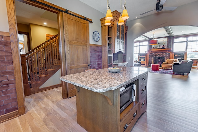 kitchen featuring a brick fireplace, light wood-type flooring, stainless steel microwave, hanging light fixtures, and a center island