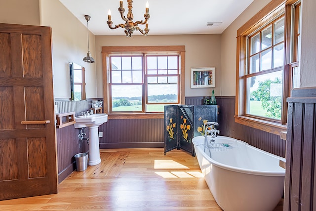 bathroom featuring wood-type flooring, a chandelier, a washtub, and a wealth of natural light