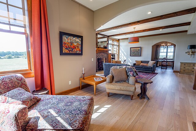 living room featuring a brick fireplace, beamed ceiling, and light wood-type flooring