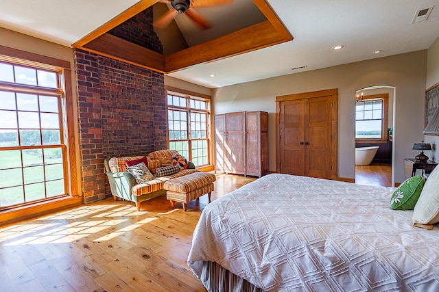 bedroom featuring ceiling fan, light wood-type flooring, brick wall, and multiple windows