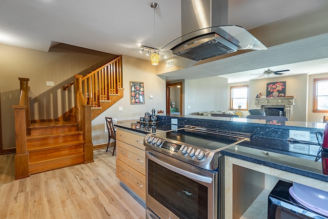 kitchen featuring stainless steel electric stove, light brown cabinets, light hardwood / wood-style floors, island range hood, and dark stone counters