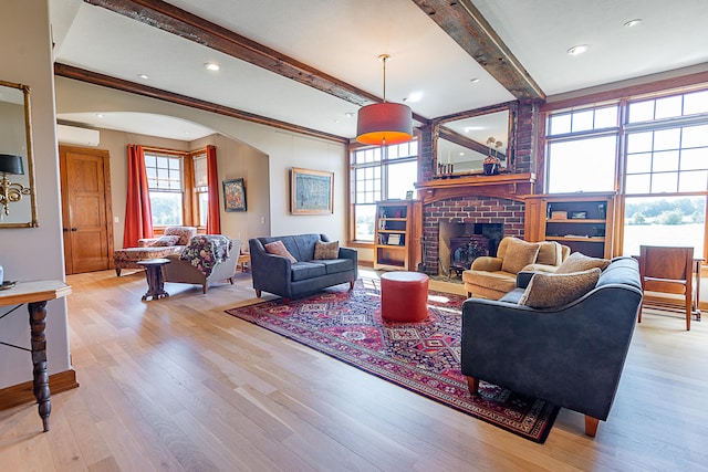 living room with a brick fireplace, beamed ceiling, a wall unit AC, and light wood-type flooring