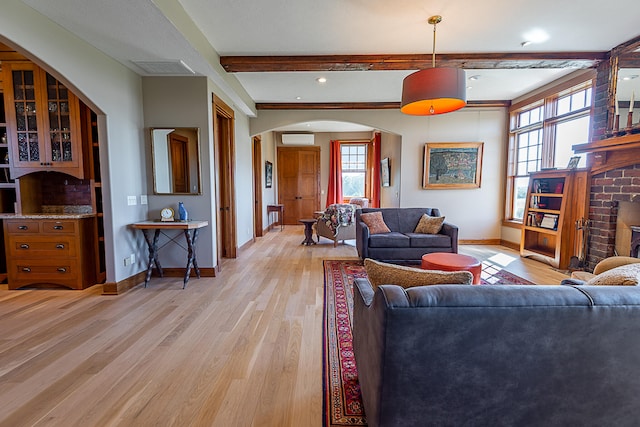 living room with a brick fireplace, beam ceiling, light hardwood / wood-style flooring, and a wall unit AC