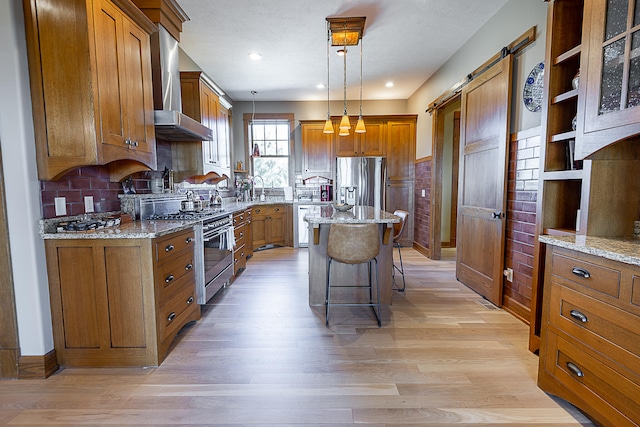 kitchen with a center island, stainless steel appliances, wall chimney range hood, a barn door, and a kitchen breakfast bar