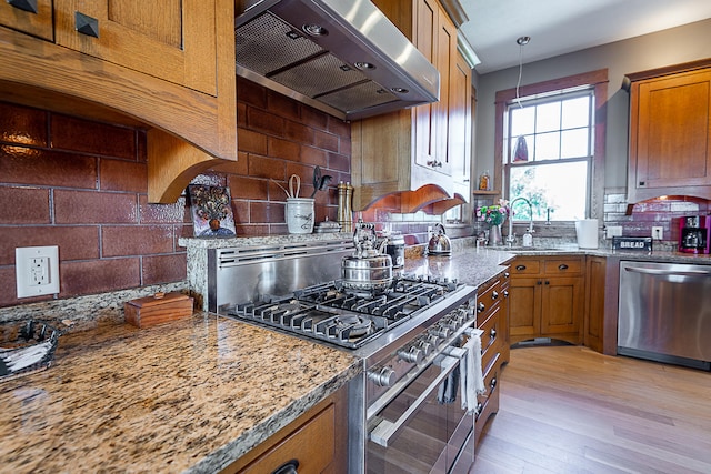 kitchen featuring light stone countertops, decorative backsplash, stainless steel appliances, ventilation hood, and light hardwood / wood-style flooring