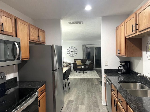 kitchen featuring dark stone counters, appliances with stainless steel finishes, sink, and light wood-type flooring