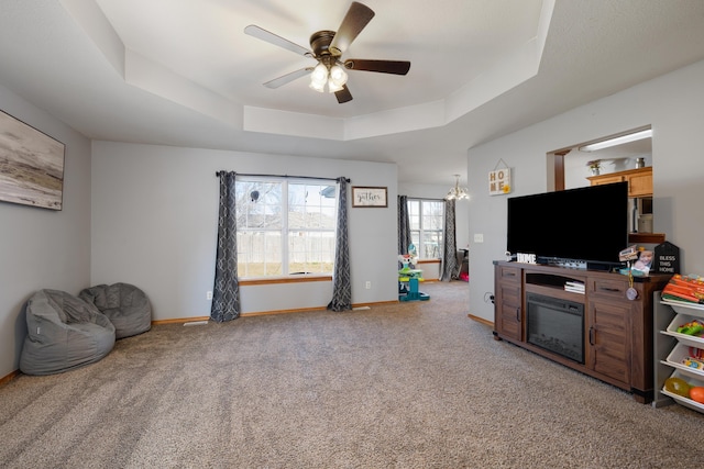 carpeted living room with ceiling fan with notable chandelier and a raised ceiling