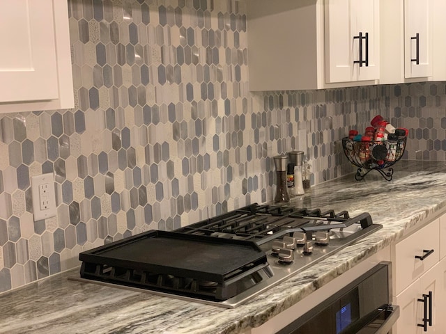 kitchen featuring light stone countertops, backsplash, wall oven, cooktop, and white cabinetry