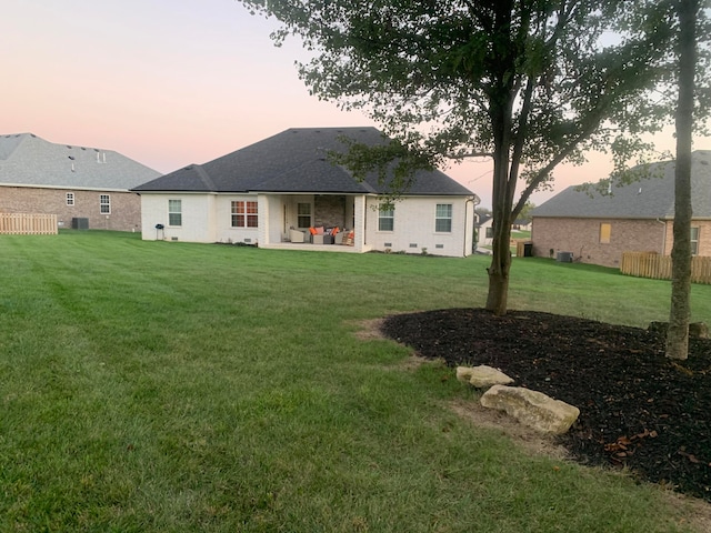 back house at dusk featuring a lawn