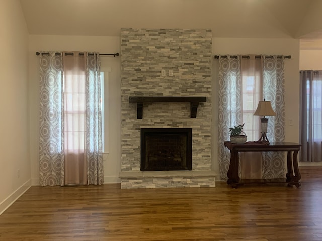 living room featuring a stone fireplace, lofted ceiling, and hardwood / wood-style flooring