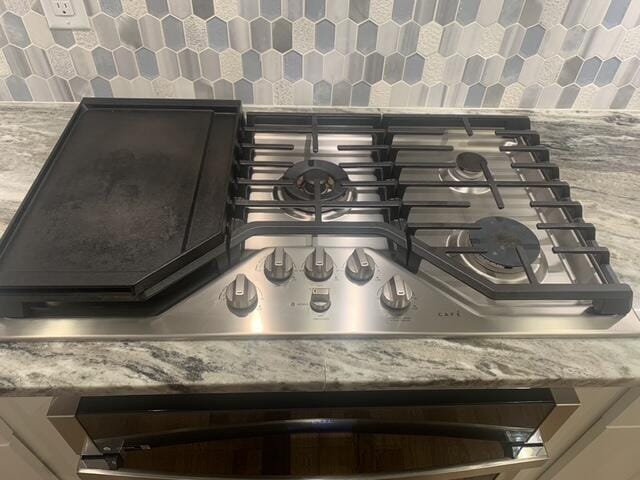 room details with decorative backsplash, light stone counters, and stainless steel gas stovetop