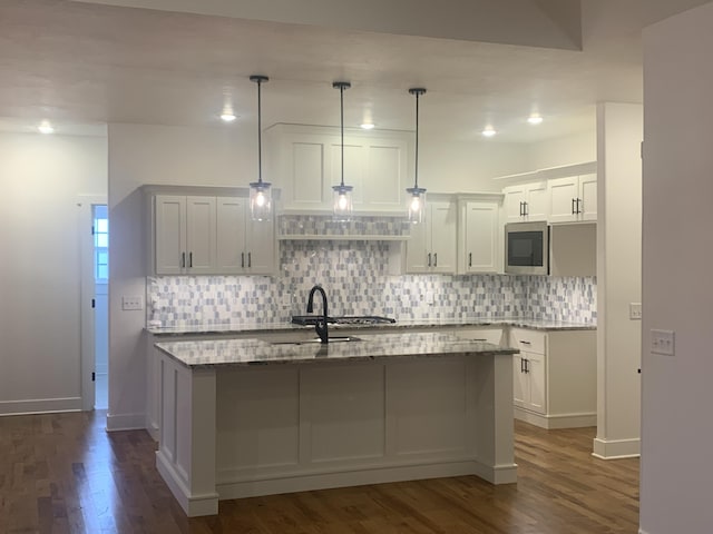 kitchen with light stone countertops, dark hardwood / wood-style flooring, pendant lighting, a center island with sink, and white cabinetry