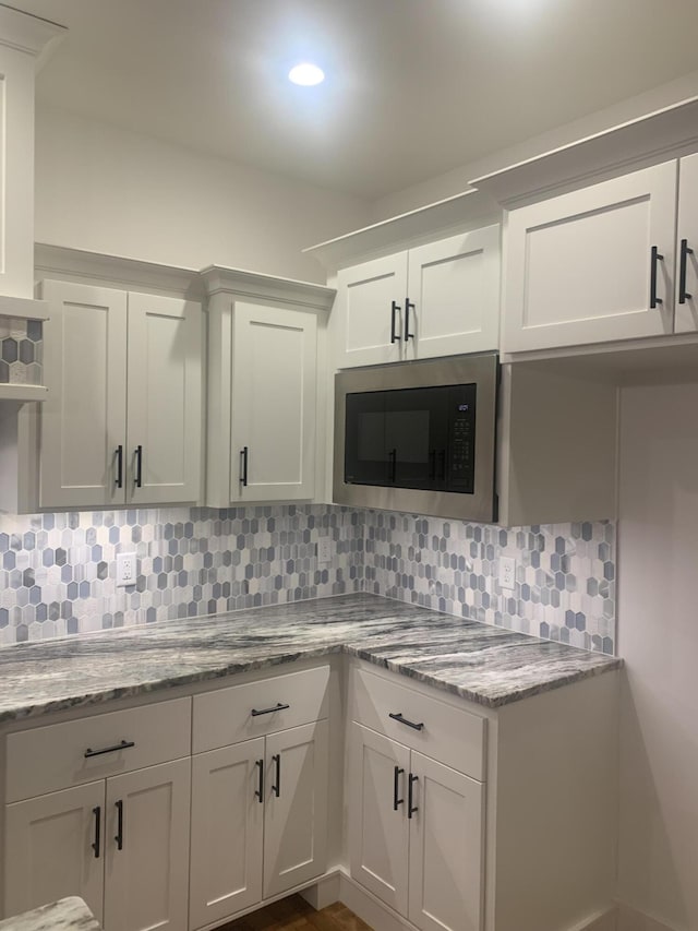 kitchen featuring white cabinetry, backsplash, built in microwave, and light stone counters