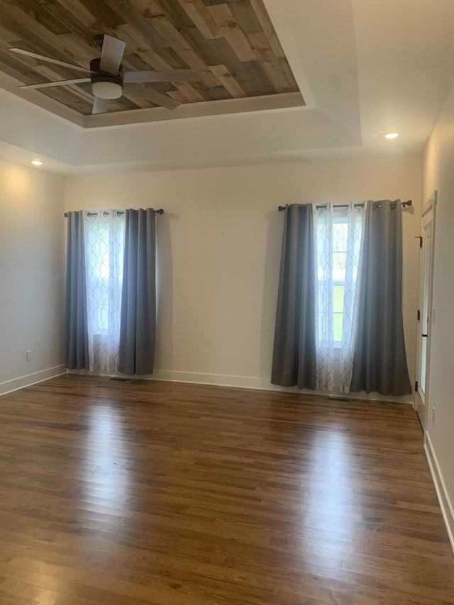 spare room featuring a tray ceiling, ceiling fan, dark hardwood / wood-style flooring, and a healthy amount of sunlight