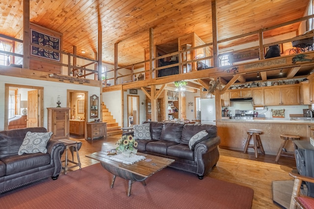 living room featuring light wood-type flooring, sink, a towering ceiling, and wooden ceiling