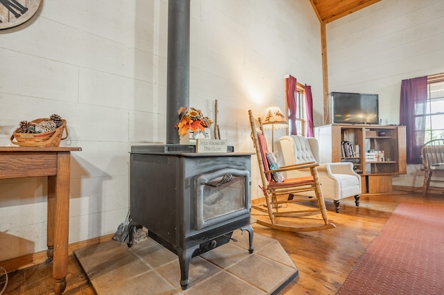 living area with a wood stove, high vaulted ceiling, and hardwood / wood-style floors