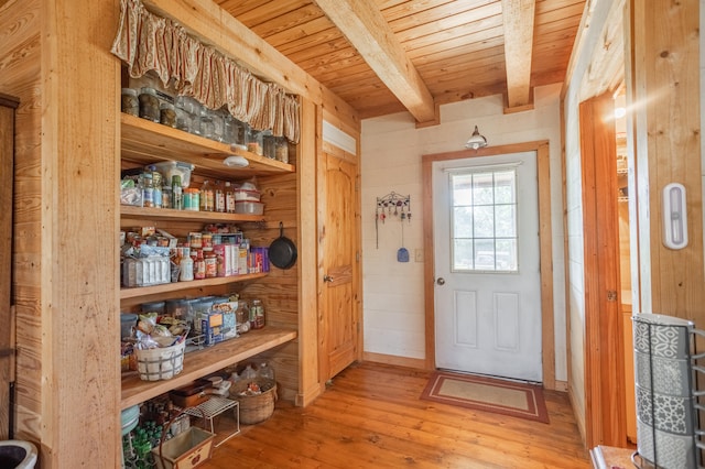 doorway to outside featuring wood walls, beam ceiling, and light wood-type flooring