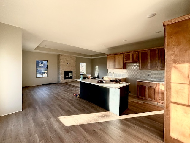 kitchen featuring a center island, tasteful backsplash, wood-type flooring, a stone fireplace, and a raised ceiling