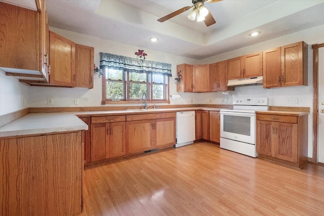 kitchen featuring light wood-type flooring, ceiling fan, white appliances, sink, and a tray ceiling