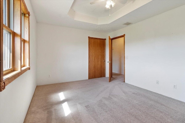 carpeted empty room with ceiling fan and a raised ceiling